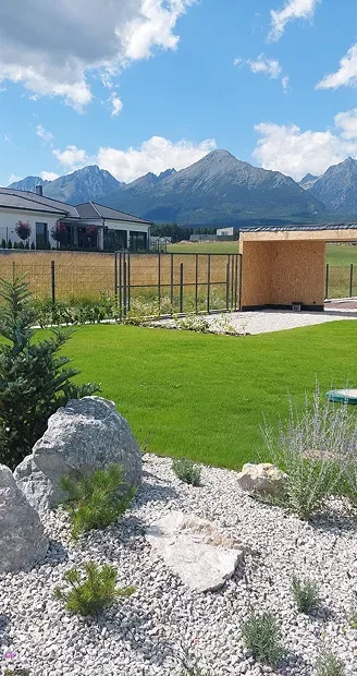Hotová skalka s kameňmi a okrasnými trávami pri trávniku, v pozadí Tatry